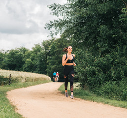 Portrait of young beautiful fit woman jogging in nature, wearing black activewear, athlete model posing outdoors, sport fashion