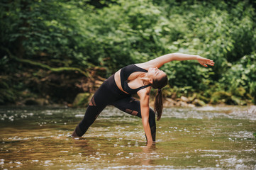 Young fit woman practicing yoga, standing in river, wearing black leggings and top