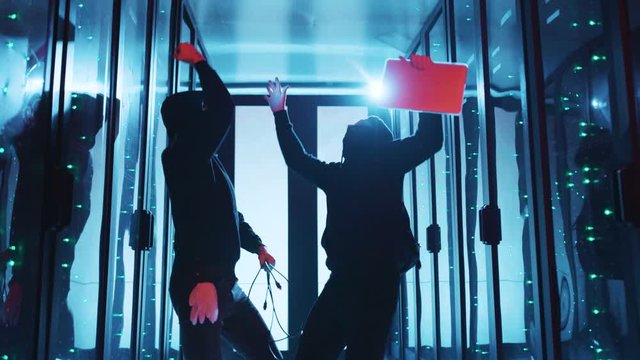 Team of successful hackers dancing in middle of server room, they breaking internet server supercomputer, having fun under red flickering lights at database. Blackout data center.