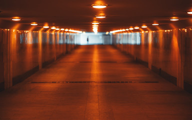 Fototapeta na wymiar View with a shallow depth of field of a long underground pass with three rows of lamps stretching into the vanishing point with a human silhouette at the end, selective focus in the foreground