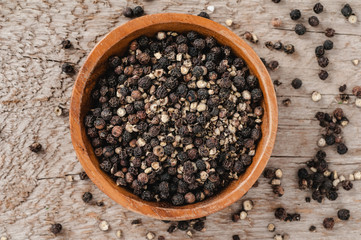 Black pepper corns in a wooden bowl on a barn board background