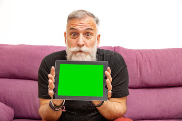 old man with white beard surprised a tablet with chromatic key background sitting on the sofa