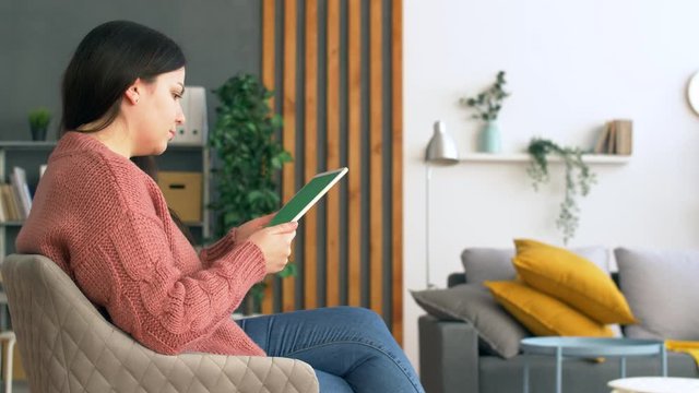 Young Ukrainian woman in modern living room hold tablet with green screen. Close up 4k commercial footage.