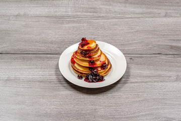 Pancakes of different sizes with jam in a white plate on a wooden background view at an angle