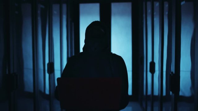 Tricky computer hacker breaking a server supercomputer, turning off lights by typing on laptop, deactivating database secure storage and laughing with success. Datacenter blackout.