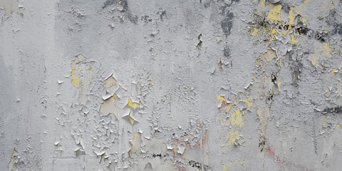 Texture of several times painted white wall with peeling paint and yellow, red and black spots of previous layers of paint. Dirty weathered shabby wall background.