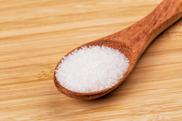 Spoon full of granulated sugar  on a wooden background