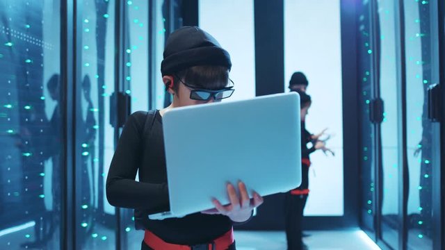 Smart boy computer spy copying data information on laptop inside database cyber security. Team of spy kids breaking into secure data center storage.