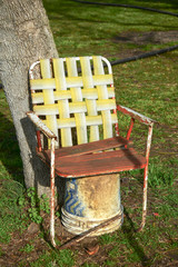 silla amarilla rota sobre balde viejo apoyada sobre un arbol