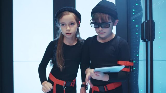 Two spy kids sneaking into server cabinet with digital laptop. Young team of professional agents children performing secret tasks with database network at data center,
