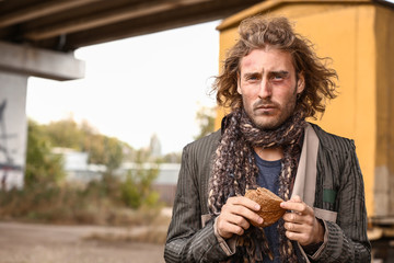 Portrait of poor homeless man with piece of bread outdoors