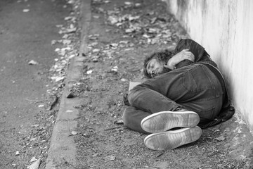 Black and white photo of poor homeless man sleeping on ground outdoors