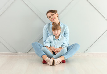 Fototapeta premium Portrait of happy mother and daughter sitting on floor near wall
