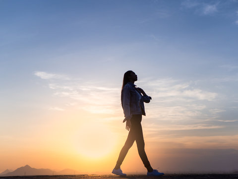 sunrise or sunset stylish adult woman walking toward the horizon with widely placed hands on background of bright sky,Romantic Girl,Blowing Long Hair.Successful.