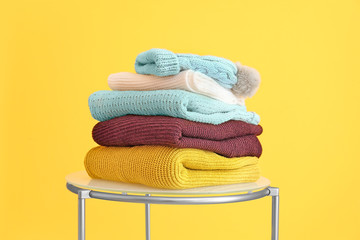 Set of warm winter clothes on table against color background