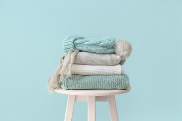 Set of warm winter clothes on table against color background