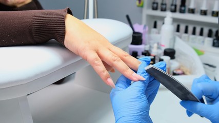 Manicurist files a nail with a nail file to a client. Manicure process, nail extension. close-up