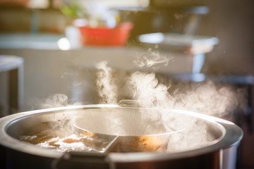 The water is boiling  in a large soup pot, there is smoke and hot spit.