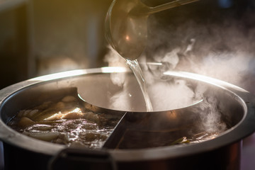 Cooking person in the restaurant is cooking while using the dipper in a large soup pot. And the water is boiling, there is smoke and hot spit.