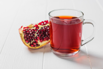 A mug of pomegranate juice and a ripe pomegranate on a white table.