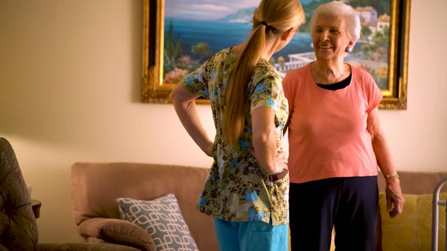 Home Healthcare Nurse Helps Elderly Woman Get Up From Couch And Walk.