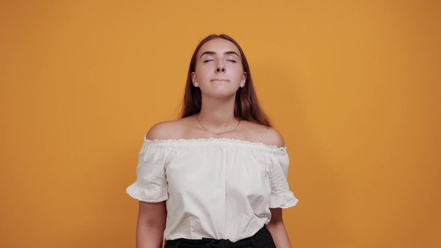 Attractive young woman spreads hands, screaming isolated on orange background in studio in casual white shirt. People sincere emotions, lifestyle concept.
