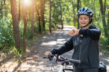 Naklejka premium Senior asian woman bicycle in the park, With checking time or heart rate from smart watch