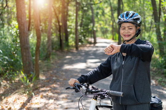Senior asian woman bicycle in the park, With checking time or heart rate from smart watch