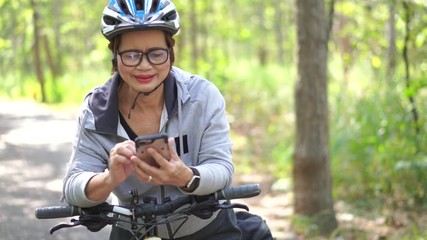 Senior asian woman bicycle in the park, With using smart phone and listening to music - Powered by Adobe