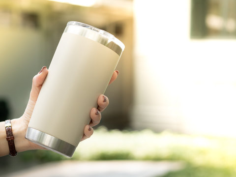 Closeup hand of a woman holding a reusable insulated stainless steel tumbler to show awareness of 'Say No to single use plastic’ and ‘Zero Waste’ in outdoor area of cafe.