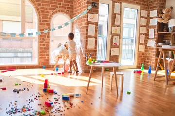 Beautiful african american toddler standing and smiling around lots of toys at kindergarten