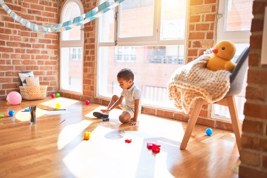 Beautiful african american toddler playing with cars around lots of toys at kindergarten