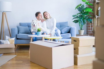 Fototapeta na wymiar Young beautiful couple with dog sitting on the sofa at new home around cardboard boxes