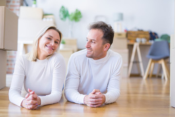 Obraz premium Young beautiful couple lying down on the floor at new home around cardboard boxes
