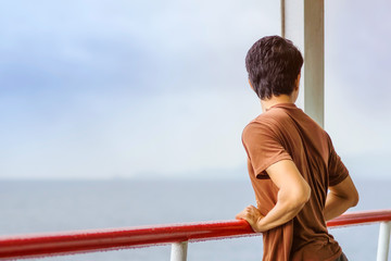 Asian man stands on baluster of ferry for relaxing and look at the ocean and island.