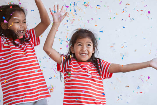 Cute asian child girl and her sister play with colorful confetti together to celebrate in their party with fun