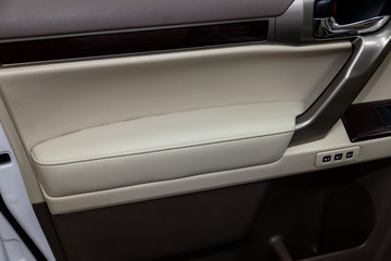 The interior of the car with a view of the drivers door with buttons, armrest and light beige leather after detailing and dry cleaning
