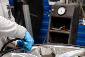 A car repair and maintenance specialist in blue rubber gloves pumps a vehicle wheel with a hose under air pressure. Auto service industry.