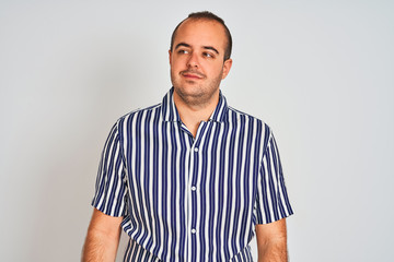 Young man wearing blue striped shirt standing over isolated white background smiling looking to the side and staring away thinking.