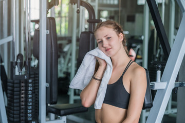 Fototapeta na wymiar Sports tired woman after exercise wipes sweat on face in fitness gym sport club