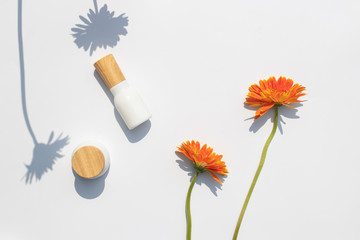 Top view of white cosmetic bottle containers with Gerbera flowers and with shadow of flower on white background.