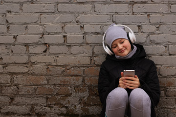 A teenager listens to music on headphones and holds a telephone