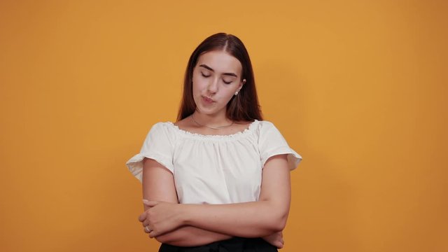 Resentful young woman blowing lips isolated on orange background in studio in casual white shirt. People sincere emotions, lifestyle concept.