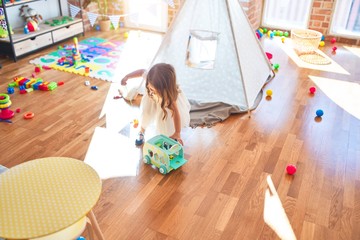 Adorable blonde toddler playing around lots of toys at kindergarten