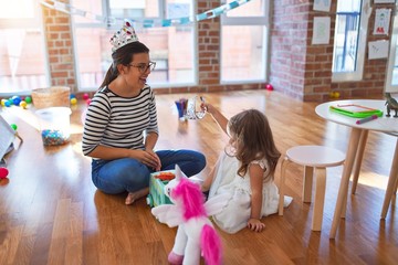 Beautiful teacher woman and toddler wearing princess crown playing around lots of toys at kindergarten © Krakenimages.com