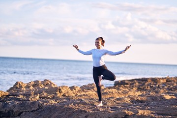 Young beautiful sportwoman smiling happy practicing yoga. Coach with smile on face teaching tree pose at the beach