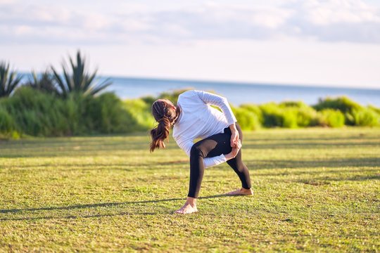 Young beautiful sportwoman practicing yoga. Coach teaching revolved triangle pose at park