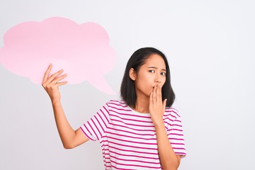 Young chinese woman holding cloud speech bubble standing over isolated white background cover mouth with hand shocked with shame for mistake, expression of fear, scared in silence, secret concept