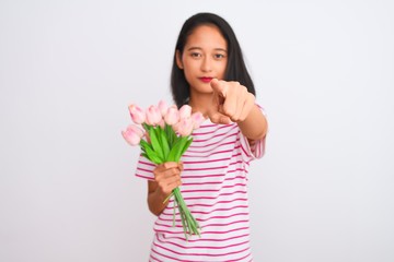 Young chinese woman holding bouquet of roses standing over isolated white background pointing with finger to the camera and to you, hand sign, positive and confident gesture from the front