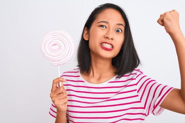 Young beautiful chinese woman eating lollipop standing over isolated white background annoyed and frustrated shouting with anger, crazy and yelling with raised hand, anger concept